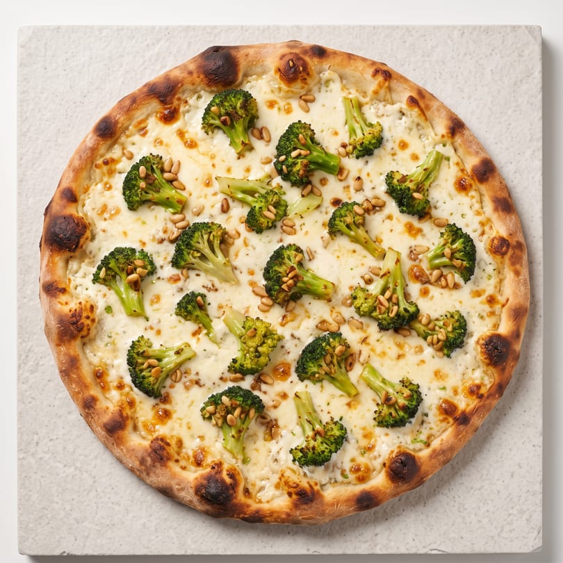 A white pizza with broccoli florets and pine nuts on a light gray square plate.
